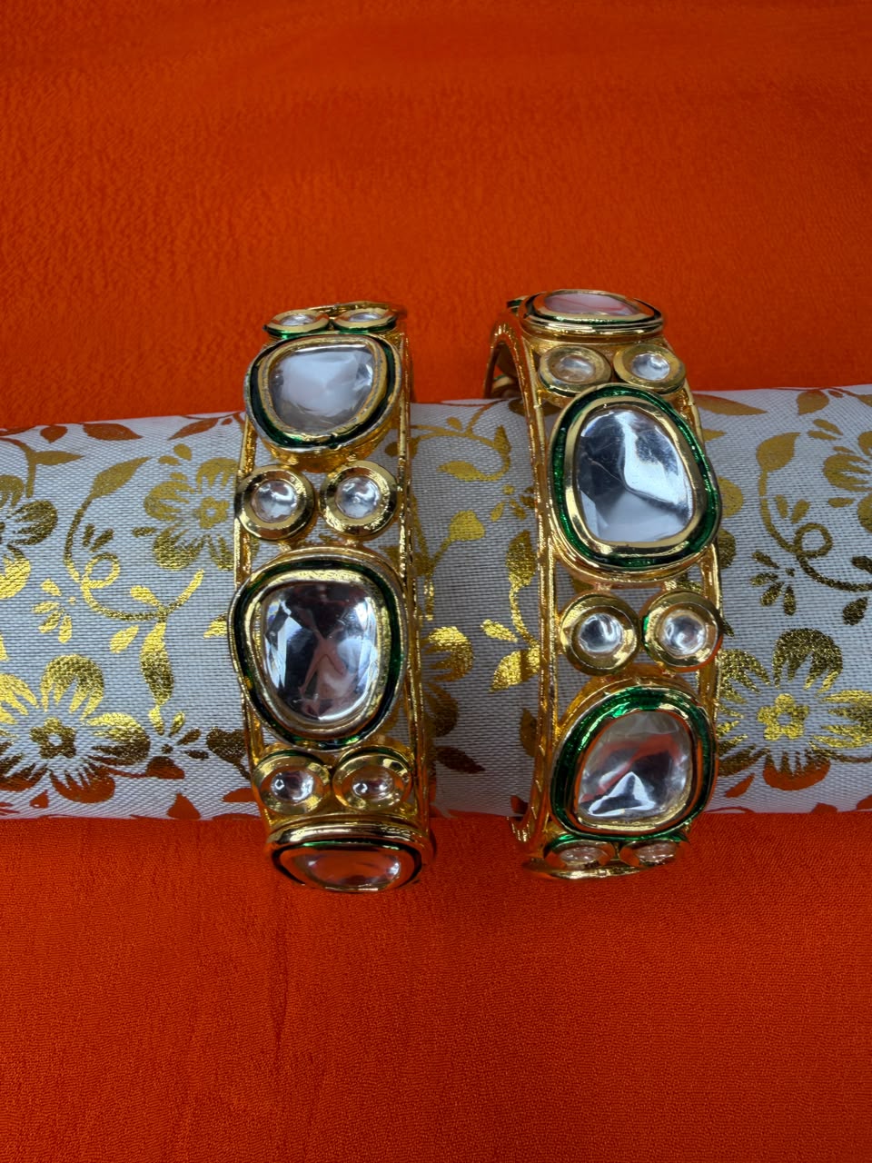 Pair of wide gold tone kundan bangles with clear stones and green enamel accents