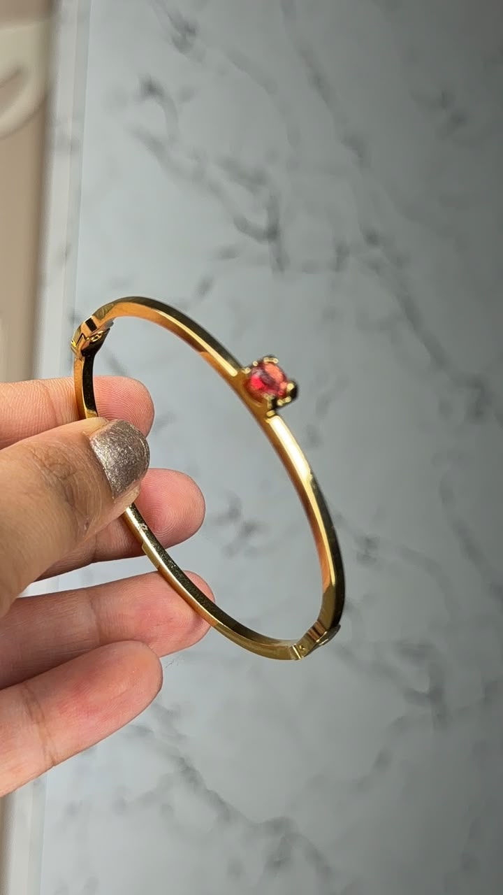Minimal gold tone bangle with ruby red solitaire stone