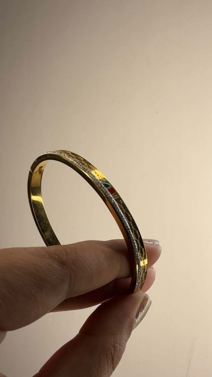 Slim gold tone bangle with two-tone detailing and small colored enamel accents